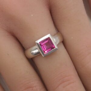 Silver ring with a square-cut pink gemstone worn on a finger, close-up view