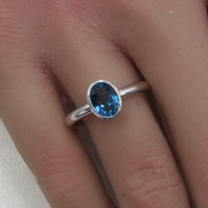 Silver ring with a oval blue gemstone worn on a finger, close-up detail showing facets.