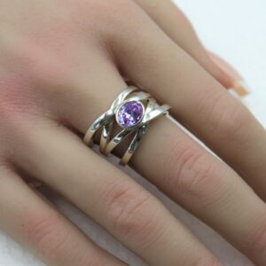 Close-up of a silver ring with a purple gemstone on a finger.