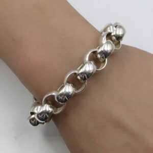 Close-up of a silver chunky chain bracelet resting on a tan forearm.